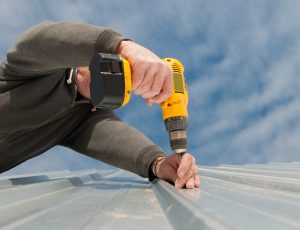 man using drill to install a tin roof